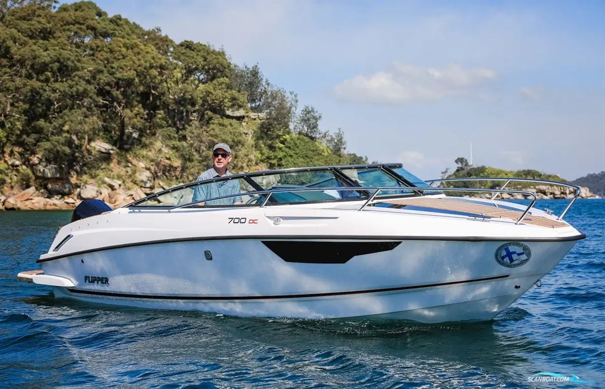 A man steering a Flipper 700 DC boat on calm waters, surrounded by green hills and blue sky.